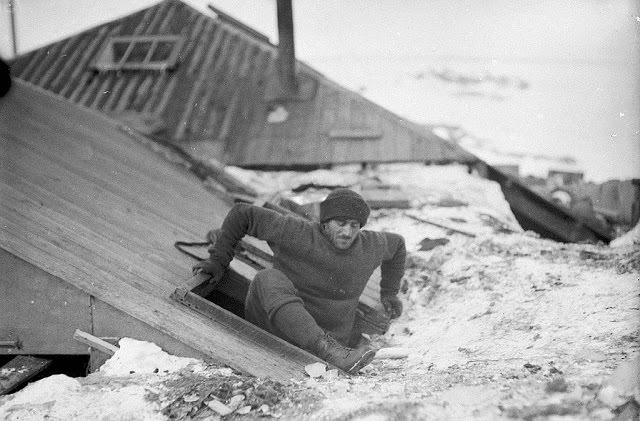 Mertz leaving the hut by the trapdoor on the verandah roof, 1912
