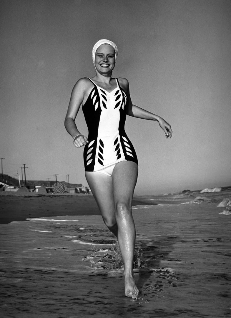 Actress Alexis Smith in a swimming costume running along the beach in southern California, 1940