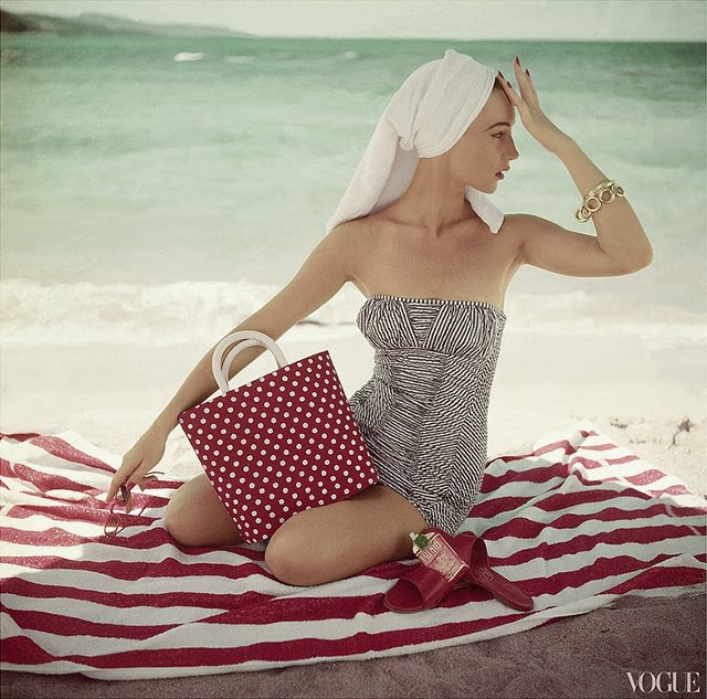 Model seated on striped beach towel wearing grey and white patterned strapless bathing suit, 1954