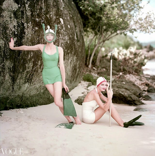 Two models in Rose Marie Reid swimsuits. Model on left stands tree wearing blue suit, mask and flippers; model on right wears white suit with matching cap, and flip