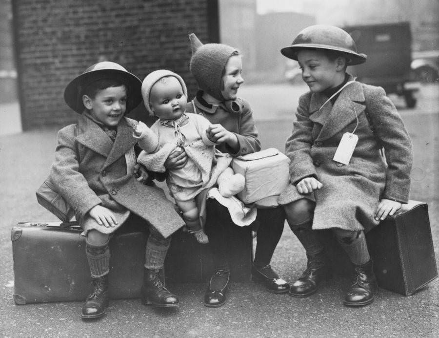 Three young evacuees sit on their suitcases ready for their journey away from the danger of the city. England. 1940.