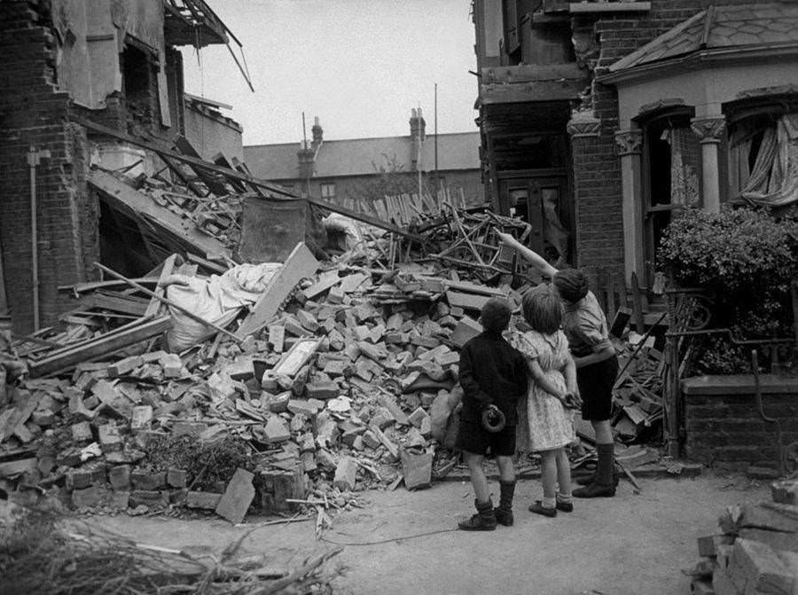 A homeless boy points out his bedroom to his friends after his home had been wrecked during a random bombing raid in an eastern suburb of London, 1940.