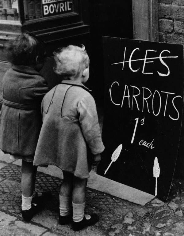 Two little girls read a board advertising carrots instead of ice pops, 1941.