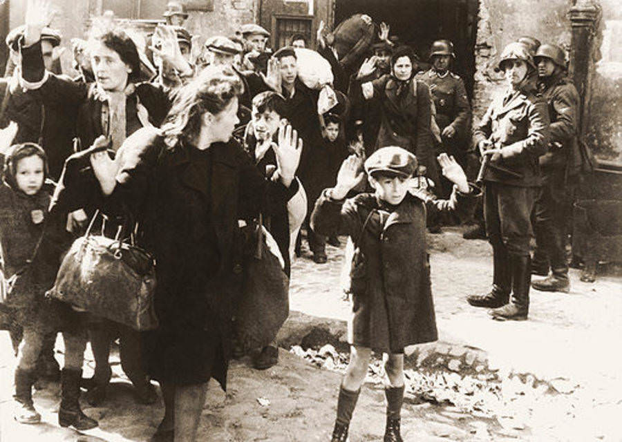 A Jewish boy raises his hands at gunpoint after Nazi SS soldiers forcibly removed him and other ghetto residents from the bunker, 1943.