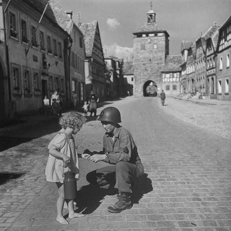 American Supply Sergeant Ralph Gordon kneels in a street to give a piece of gum to a barefoot German girl, 1945.