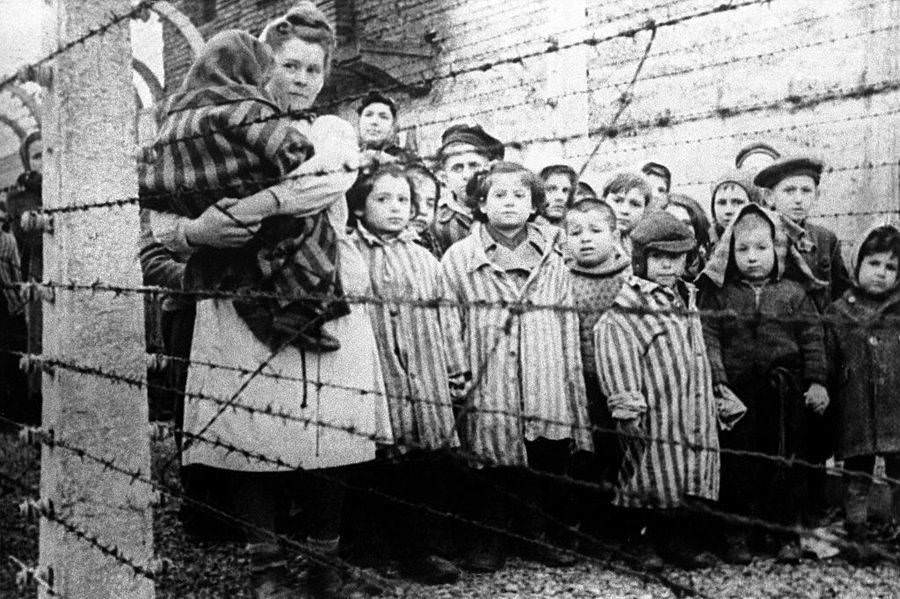 Child survivors of the Auschwitz concentration camp stand near the fence , 1945.