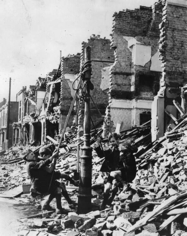 Young boys swing from a lamp post in the midst of rubble left by a bombing raid on London during the Blitz, 1940.