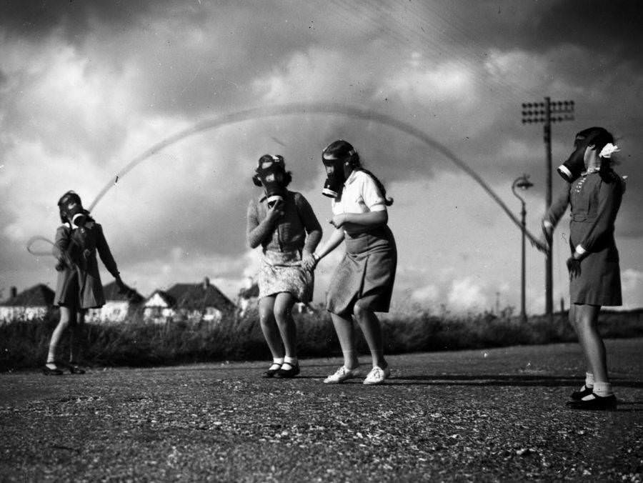 London children wear their gas masks as they skip in the park at their temporary homes on the south coast of England. 1940.