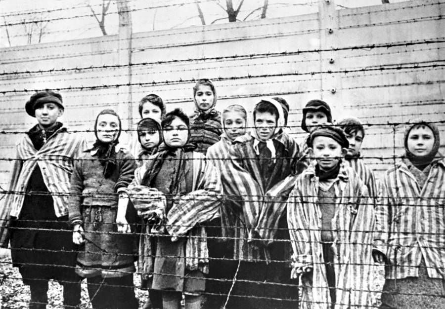 A group of child survivors stand behind a barbed wire fence at the Auschwitz-Birkenau concentration camp in southern Poland, 1945.