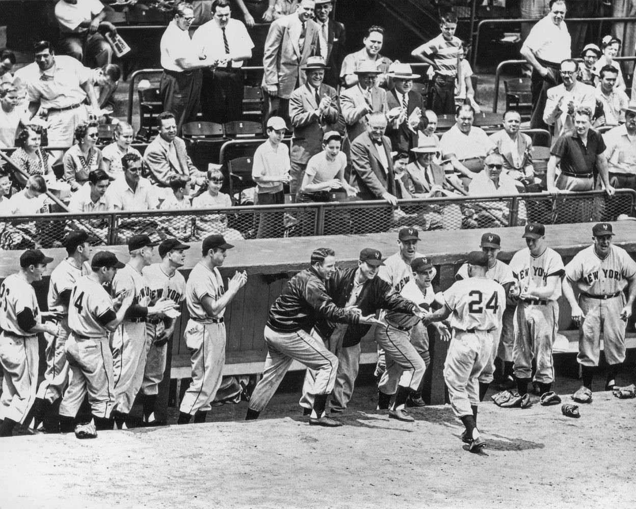 Teammates and fans applaud and reach out the shake the hand of American baseball player Willie Mays of the New York Giants after a home run in the 1950s