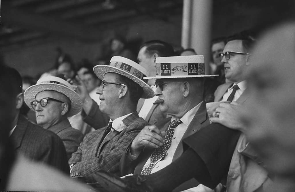 Fans watching the opening game at Candlestick Park wearing commemorative hats, 1960s