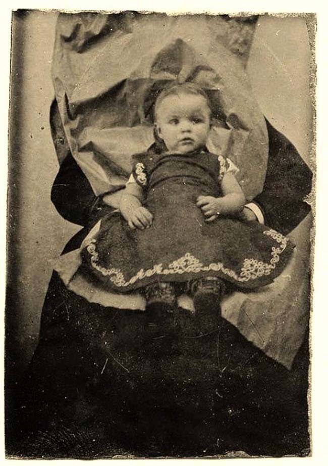 A little girl sitting on someone's lap. The person held her in place while the photo was taken.