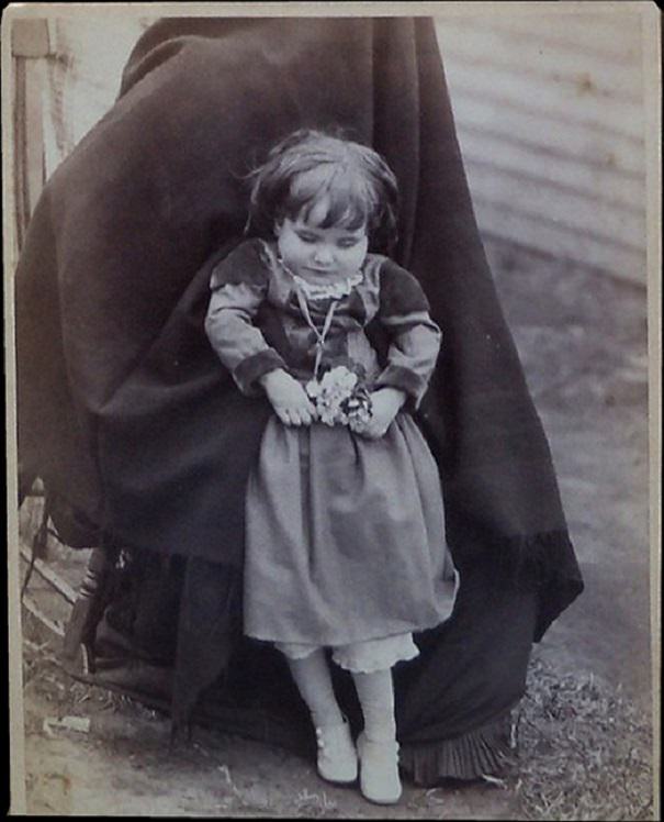 Little girl held in a standing position. The photo is a cabinet card from Villisca, Iowa taken in 1890.