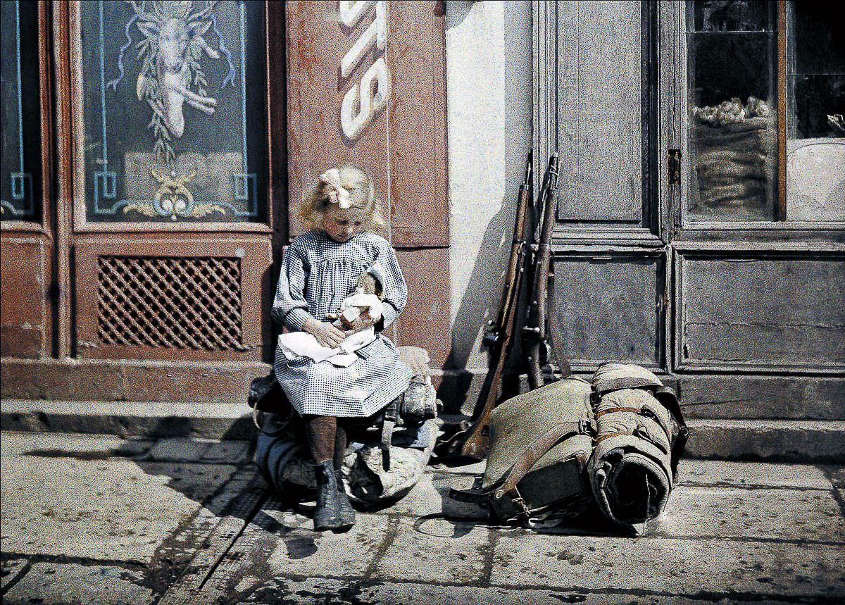 A girl holds a doll next to soldiers' equipment in Reims, France, 1917