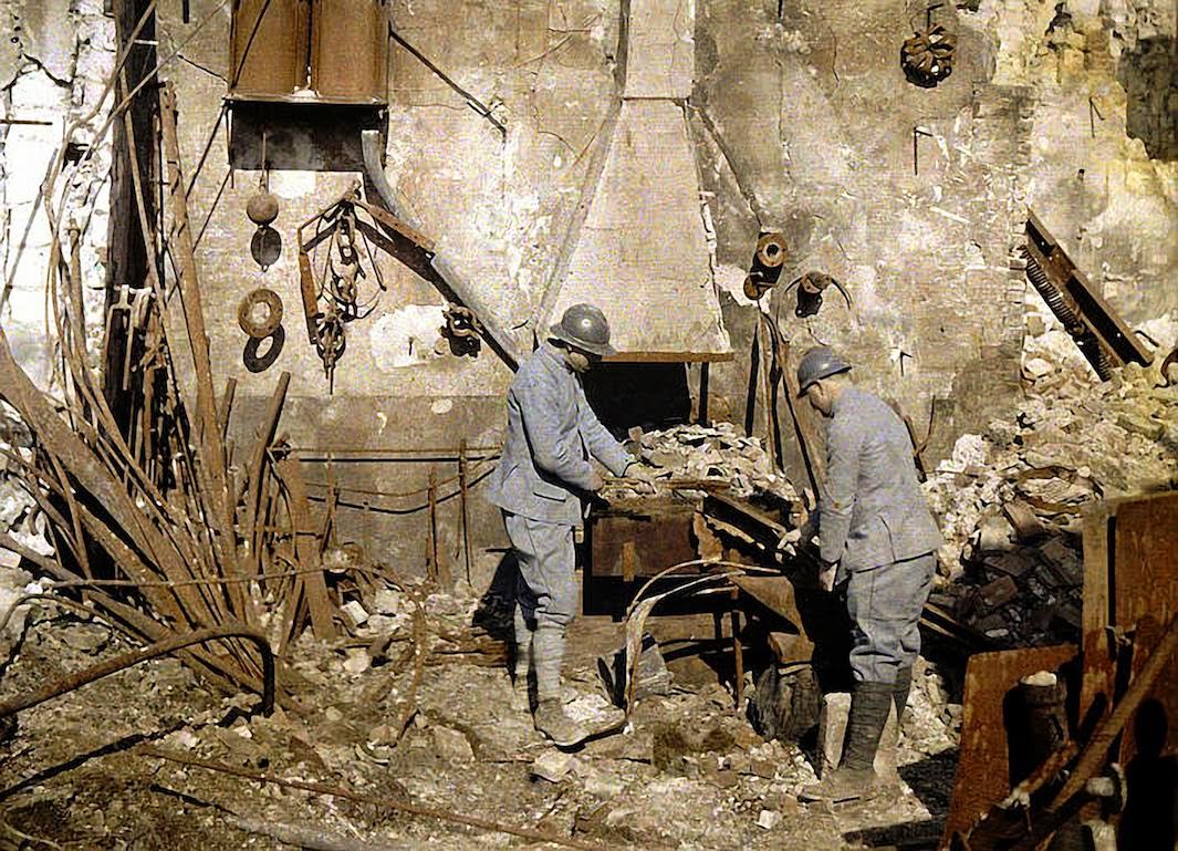 Two French soldiers work at a smith’s hearth in a forge destroyed by grenades, 1917.