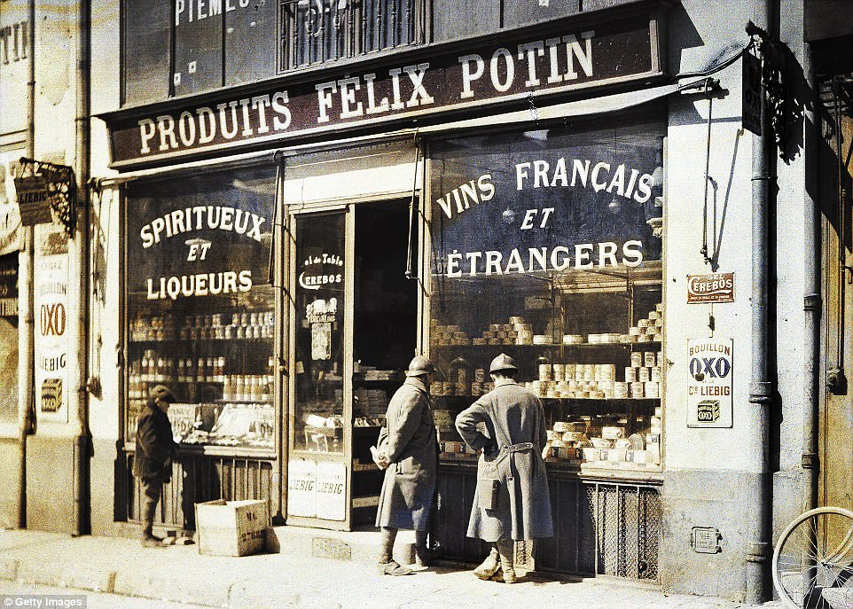 Two French soldiers and a young boy look through the window of a shop selling alcohol in Reims, France, in 1917