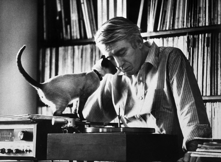 Poet Rod Mckuen Playing Record On Stereo Set While Pet Siamese Cat Nuzzles His Face Affectionately, 1967