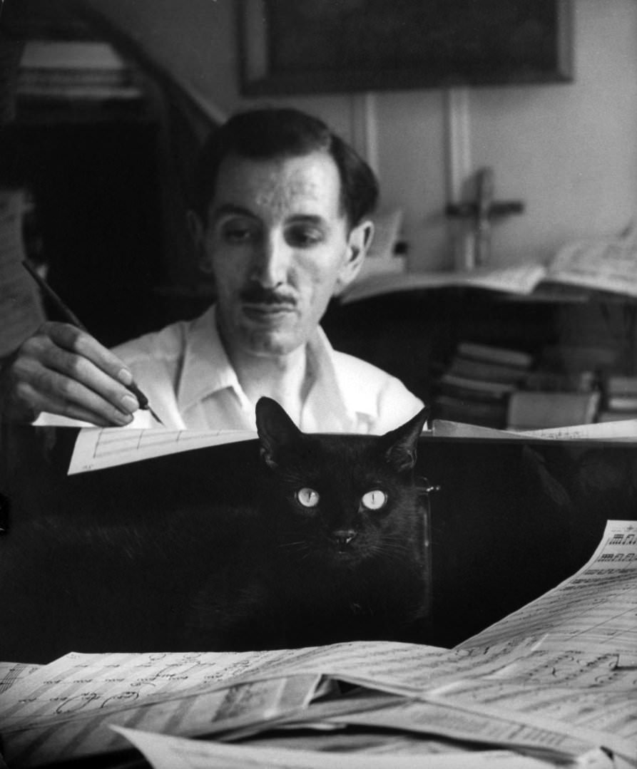 Composer Alan Hovhaness, Working In Score-Littered Studio With A Black Cat Nestling Amongst The Papers On The Piano