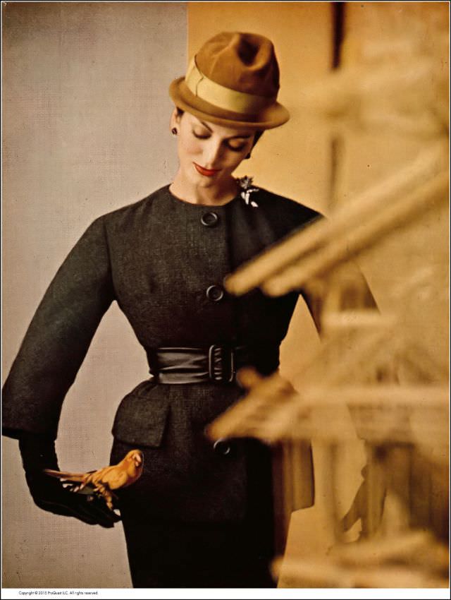 Carmen in smoky charcoal suit of British wool tweed, tunic jacket is collarless and belted in black kidskin, by Ben Zuckerman, hat by Emme, 1959.