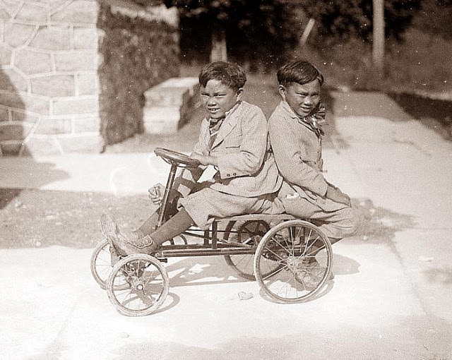 Twin boys on a small pedal car, 1920