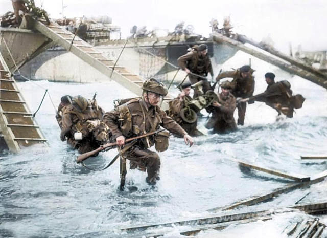 Royal Marines descend from landing craft with their heavy backpacks, weapons and equipment on Juno beach.