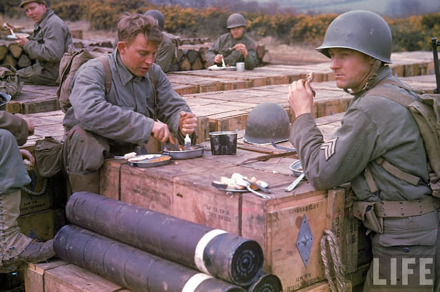 American combat engineer soldiers eating meals atop boxes of ammunition being stockpiled for the impending D-Day invasion of France.