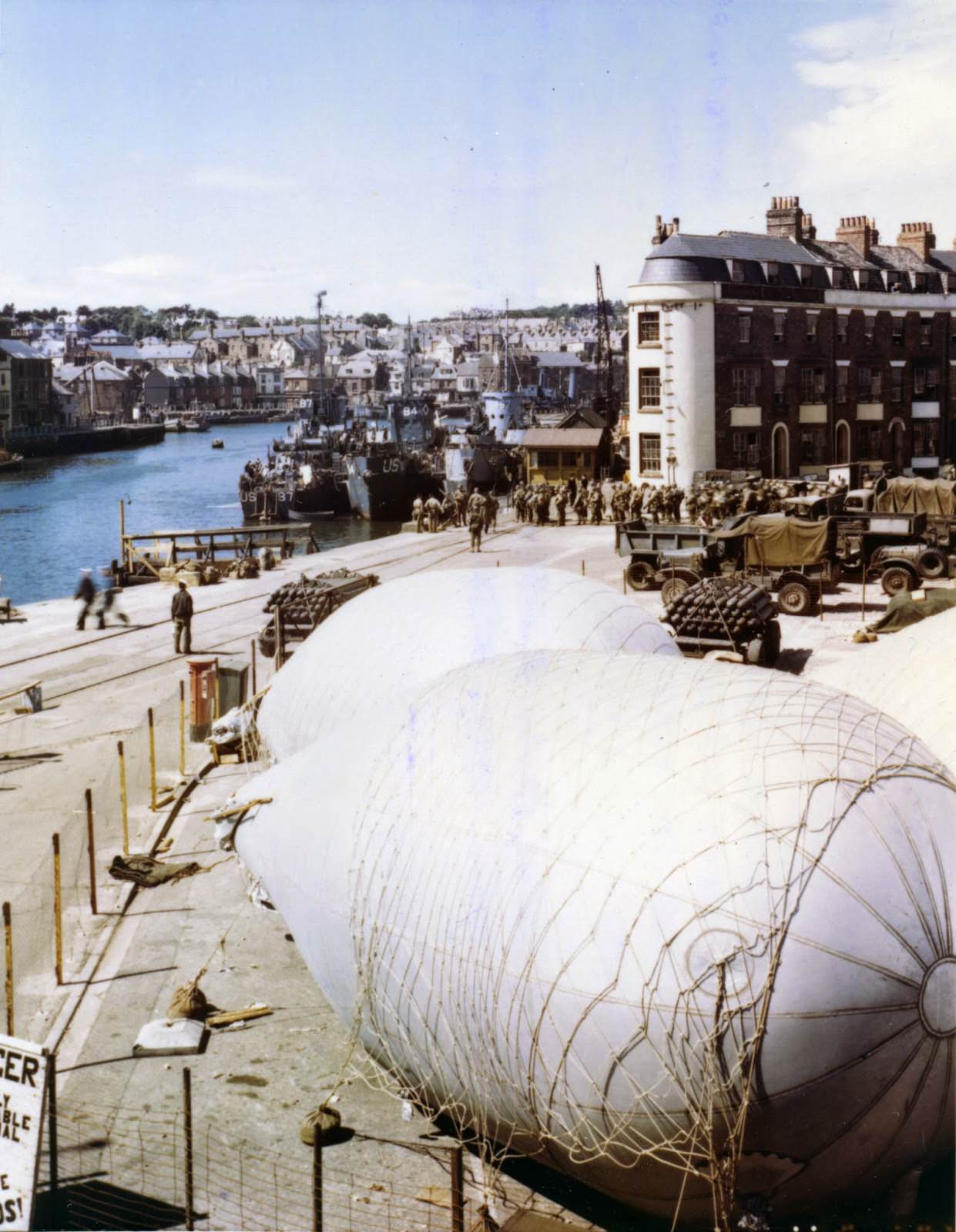 American troops load onto LSIs at a port in Britain where barrage balloons have been anchored for protection against strafing and low level bombings.