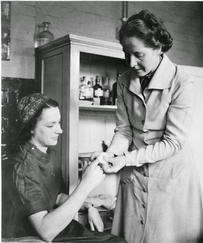 Betty Pridie receives some first aid for a sore finger from her female supervisor in Slough Training Centre's medical room, 1941.