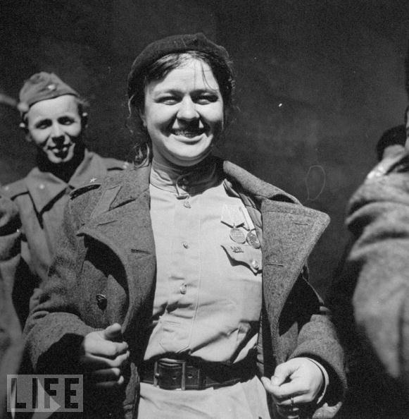 A female Russian soldier grins broadly while showing off her medals and a US Army Officer's insignia pinned to her shirt after the Allied troops met following the fall of Berlin.