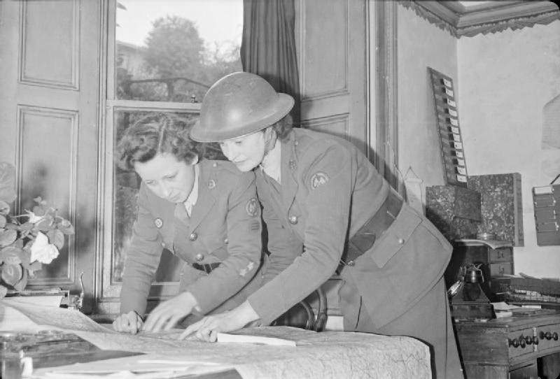 Before they leave the depot to attend an incident, women of the American Ambulance Great Britain look at a map to plan their route. A telephone call has just been received to say that several of their ambulances are needed, 1944.