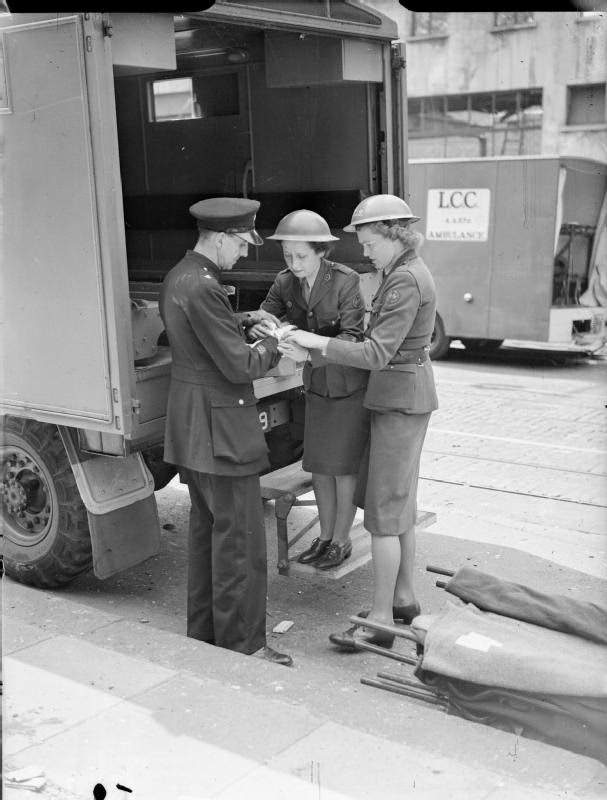 A police officer has his hand bandaged by women of the American Ambulance Great Britain following a V1 attack in Upper Norwood. The original caption states that the policeman's hand was injured by flying glass, 1944.