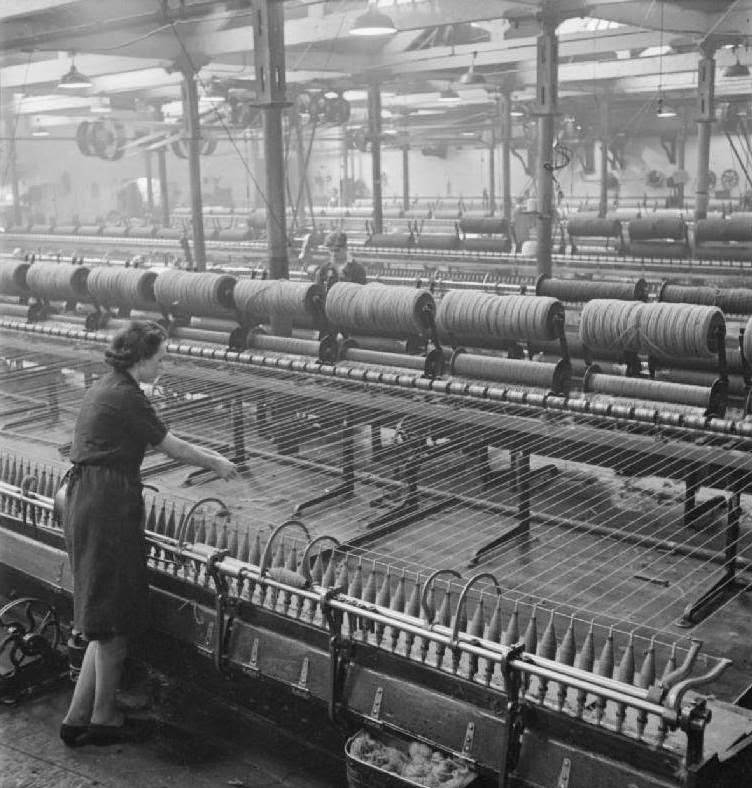 A textile worker stands at the spinning mule. The wooden rollers are transferred from the condenser to the spinning mule which is the means of twisting and stretching.