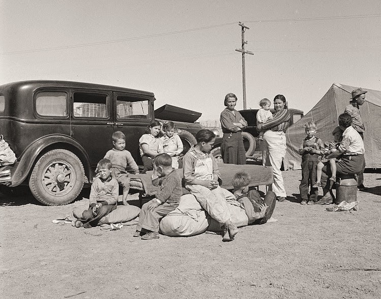 Four families, three of them related with fifteen children, from the Dust Bowl in Texas in an overnight roadside camp near Calipatria, California.
