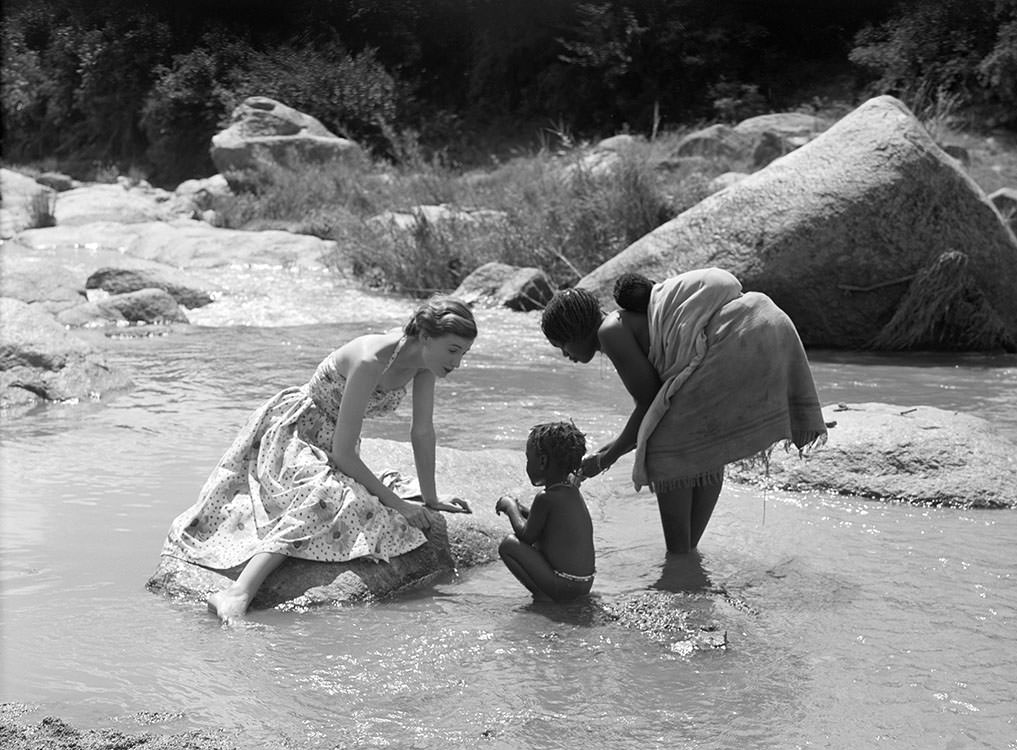Wenda Parkinson wearing a dress by Susan Small and is photographed with a mother and her children for Vogue, 1951
