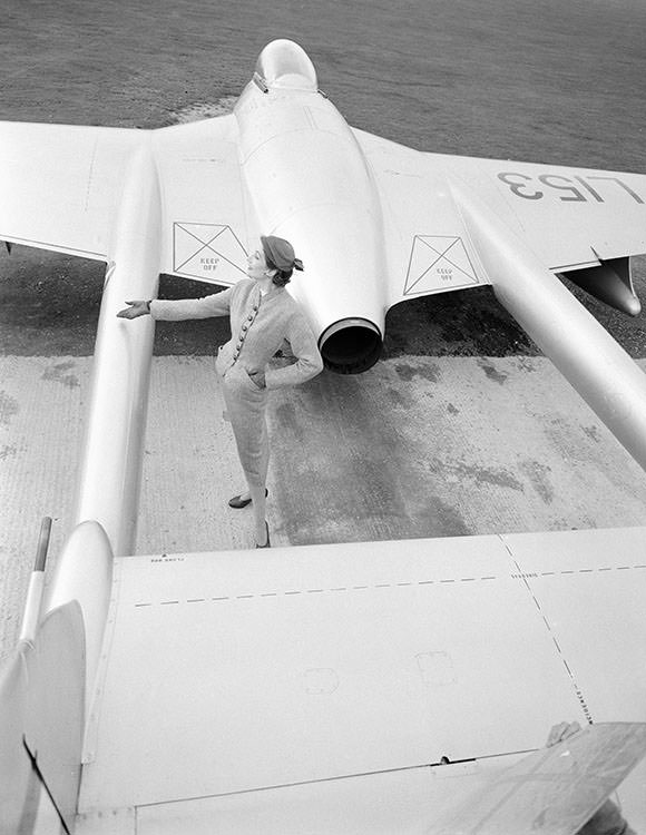 Wenda Parkinson photographed with a De Havilland ‘Vampire’ jet fighter wearing a suit and coat, 1951