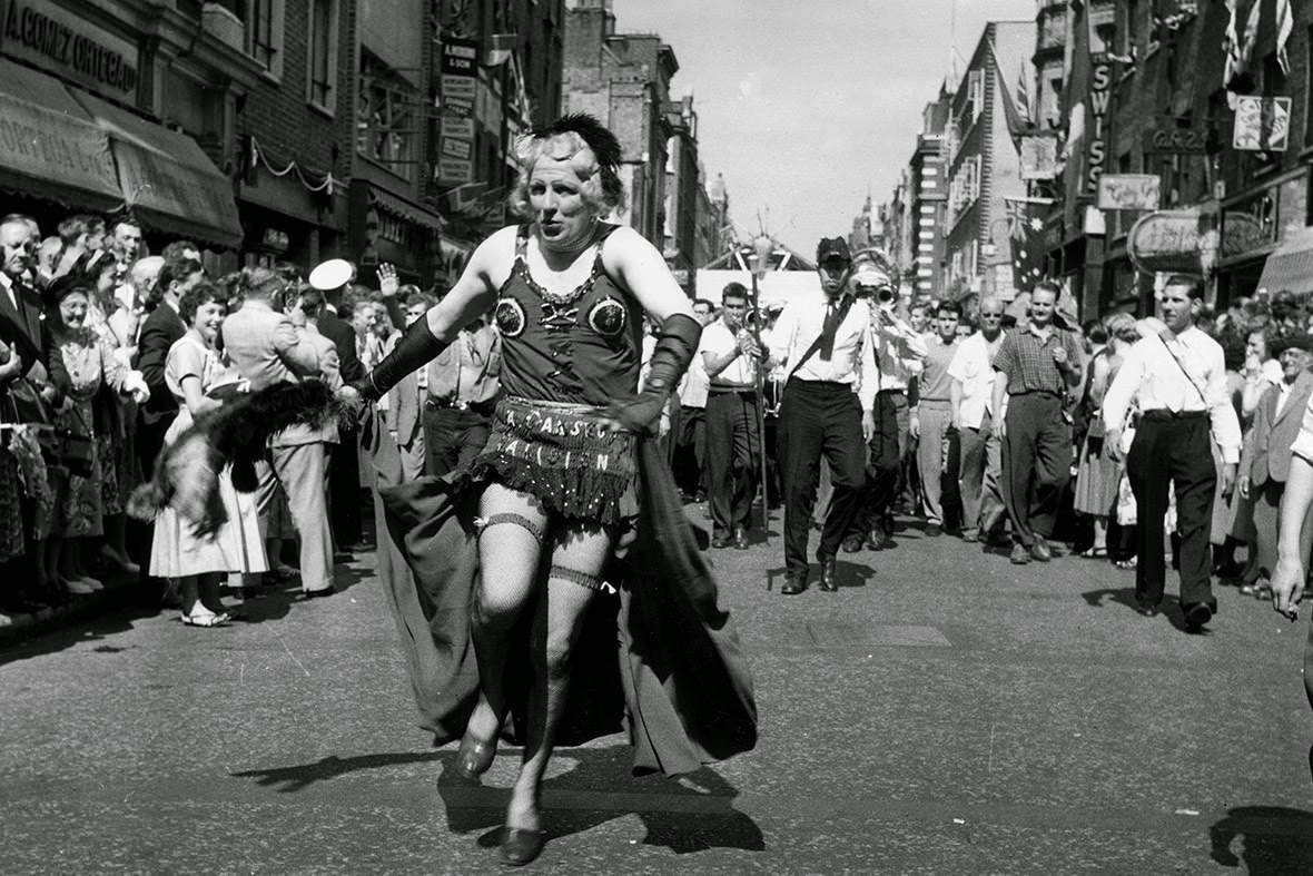 A man in drag heads a carnival procession down Old Compton Street during the Soho Fair, 1956