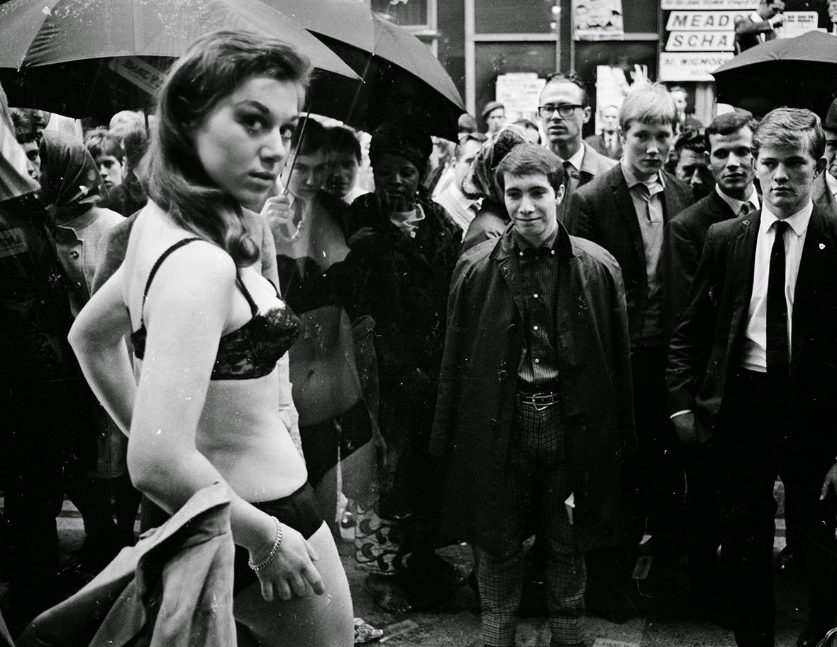 Men watch as a model takes part in a photo shoot in the window of a new Henry Moss boutique on London's fashionable Carnaby Street, 1966