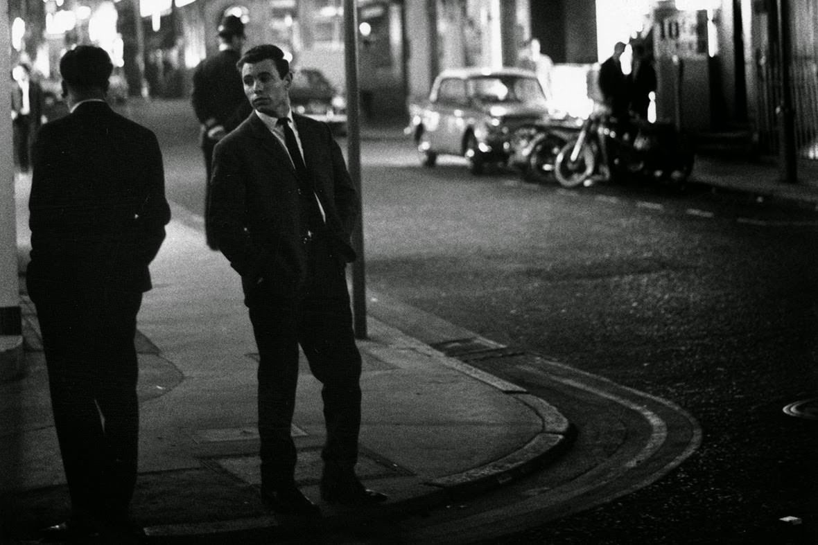 Two men look at each other while standing on a street corner in Soho, 1966