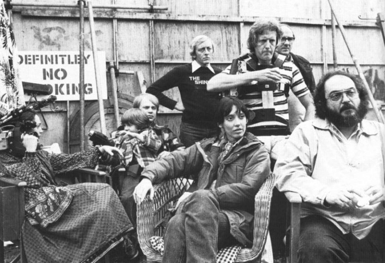 Stanley Kubrick, Shelley Duvall, Danny Lloyd sits in the lap of his on-set coach and longtime Kubrick assistant Leon Vitali. To the left, Kubrick’s daughter Vivian holds the camera she used to film the Making of The Shining documentary. Behind them, Steadicam inventor Garrett Brown stands with camer