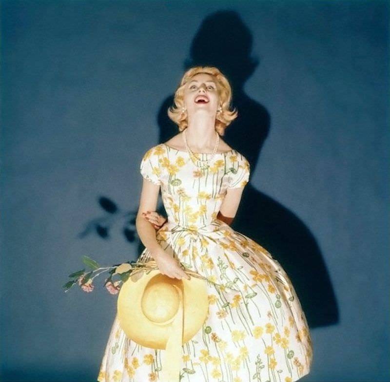 Model wearing party dress with nasturtium print on white background by Kasper of Arnold & Fox, and a straw hat by John Frederics Charmer, February 1958