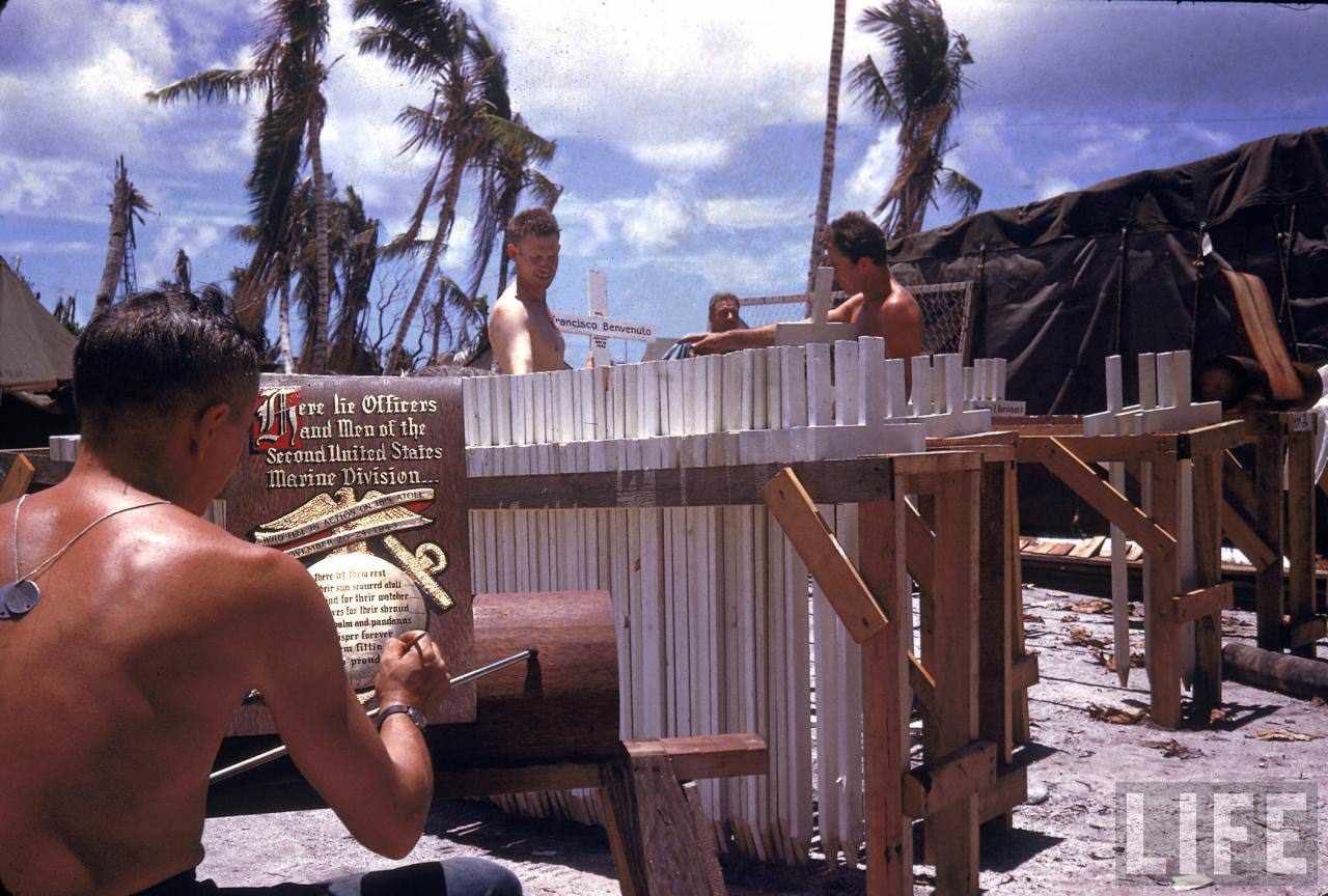 Men preparing grave markers while another finishes an ornate sign to adorn a US Marine 2 Div. graveyard on Tarawa during WWII.