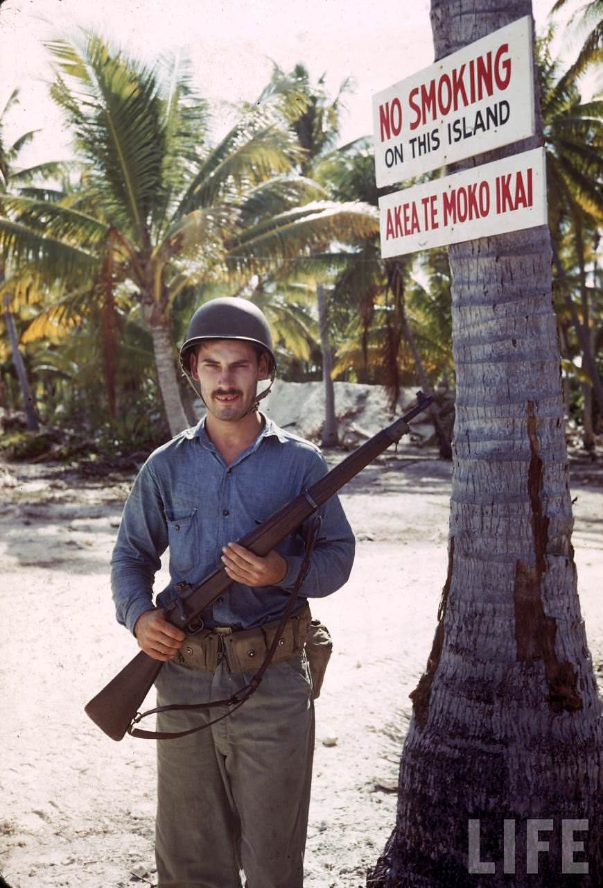 Guard on duty beneath a NO SMOKING sign on Tarawa during WWII.