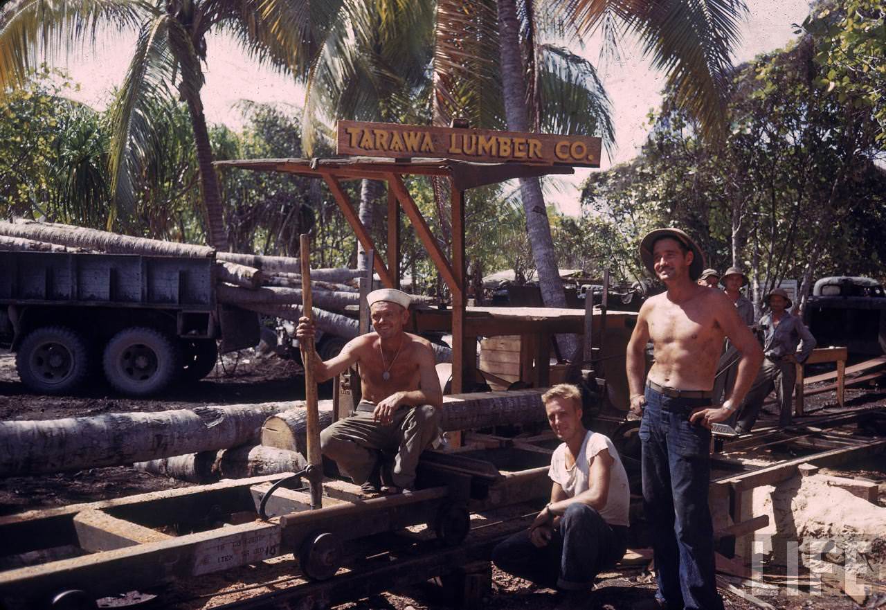 Trio of American servicemen taking a break from gathering lumber during WWII. (note sign on truck naming it the TARAWA LUMBER CO.)