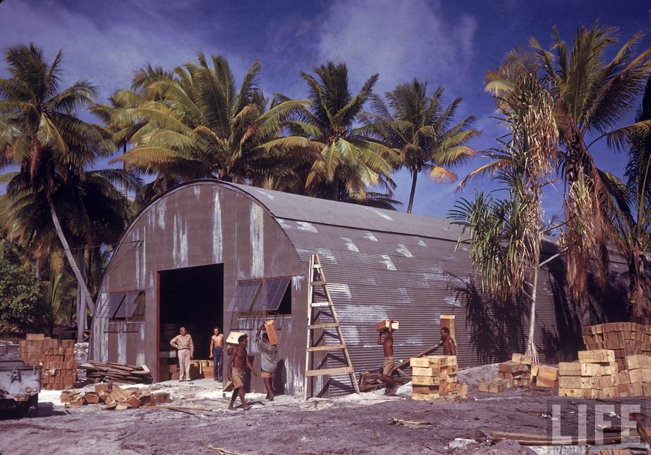 Natives carrying supplies into a quonset hut on Tarawa Island.