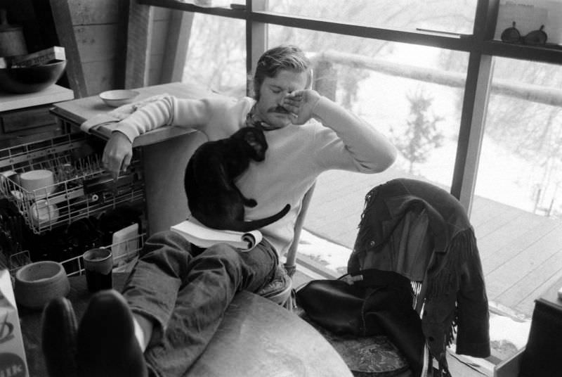 Robert Redford takes a break from reading a script with the family's cat curled up in his lap at his Utah retreat, 1969