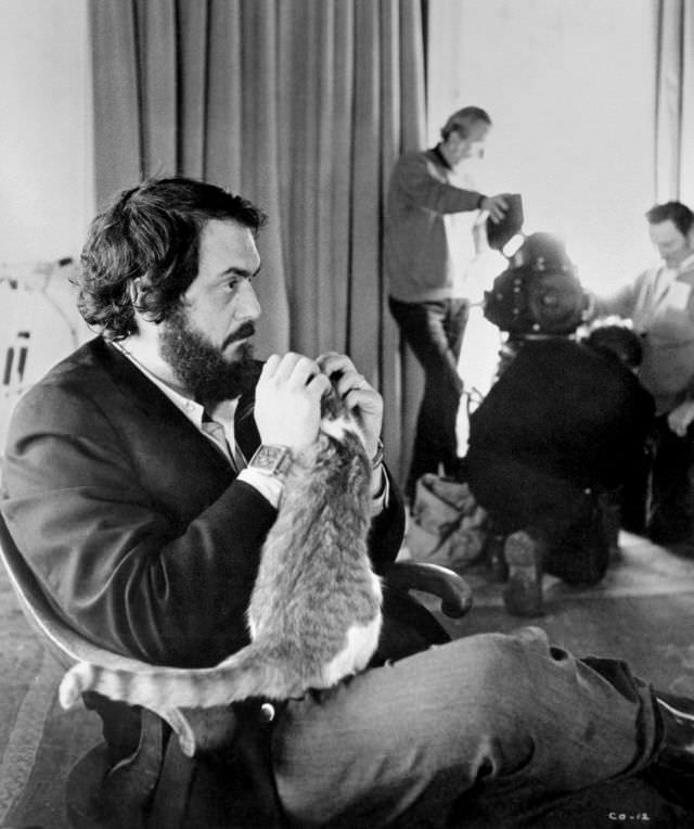 Stanley Kubrick sitting in a chair playing with a cat on the set of 'A Clockwork Orange,' 1972