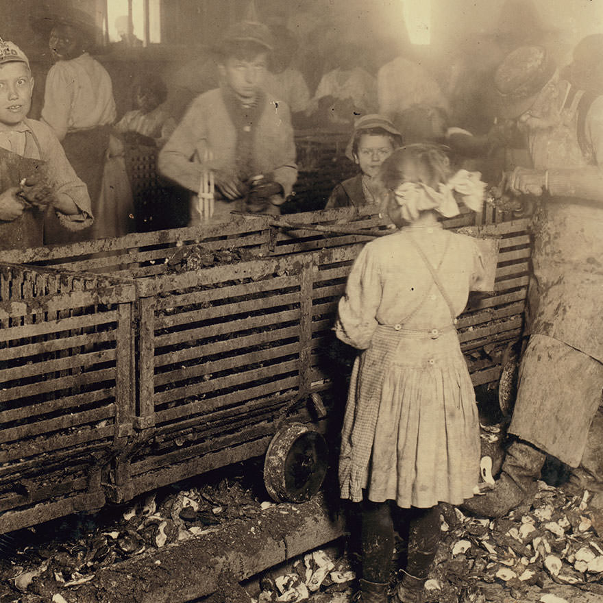 Scene in canning factory showing a 7-year old girl who shucks 3 pots of oysters a day, and works regularly, and her 6-year old brother who helps some. Mostly negro workers. The boss said “we keep only enough whites so we can control the negroes and keep them agoing.” Location: Bluffton, South Caroli
