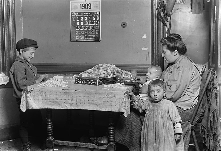 Widow & boy rolling papers for cigarettes in a dirty n.y. Tenement. Location: New York