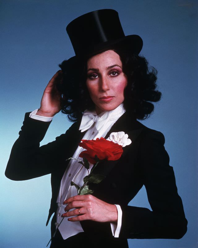 Cher, wearing a tuxedo and top hat, holds a red rose. Photo by Bettmann, 1975