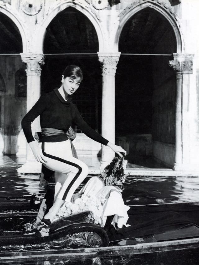 Ivy Nicholson in narrow pants and sweater shown here standing in a gondola in front of Ca' d'Oro, Venice, 1956